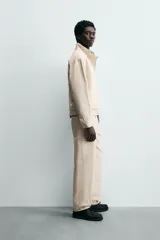 Jeans de hombre color beige claro, tiro medio, corte balloon fit con pierna relajada que se estrecha ligeramente hacia el bajo. Confeccionados en denim rígido de algodón, con cinco bolsillos y cierre frontal de cremallera y botón.