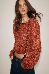 Jersey de punto grueso con textura trenzada en color naranja y bordó. Presenta cuello redondo, mangas largas abullonadas y detalle de cordones trenzados a contraste en el frente con terminación en lazada en el ruedo.
