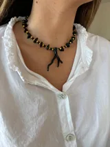 Collar corto con cuentas de piedra irregulares negras y cuentas doradas, con dije colgante en forma de rama negra.