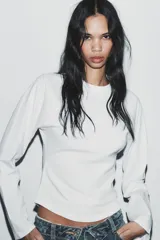 Camiseta blanca de manga larga con corte slim fit, cuello redondo y mangas ranglán. El bajo es redondeado.