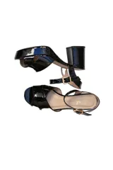 Sandalias de taco cuadrado y plataforma, confeccionadas en charol negro. Presentan tiras cruzadas en el empeine y una tira ajustable con hebilla metálica en el tobillo.