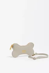 Monedero pequeño de cuero reconstituido color rojo brillante, con forma de hueso de perro. Posee cierre de cremallera dorado y una correa corta de cuero para sujetar.