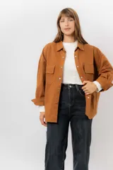 Sobrecamisa de gabardina liviana color crema, con corte oversize, cuello clásico, cierre frontal con botones a presión y dos bolsillos delanteros con solapa.