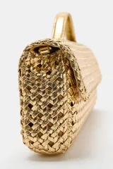 Bolso tipo sobre con diseño trenzado en color dorado. Cuenta con asa de mano fija, asa bandolera extraíble, bolsillo interior y cierre mediante solapa con imán.