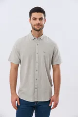 Camisa de manga corta confeccionada en mezcla de lino y algodón, con estampado de cuadros pequeños en tonos azules. Presenta cuello camisero con botones, cierre frontal abotonado, bolsillo aplicado en el pecho y dobladillo redondeado.