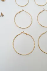 Set de siete pares de aros dorados de diversos estilos, incluyendo tres pares de aros tipo argolla de diferentes tamaños y texturas, y cuatro pares de aros pequeños con diseños variados como perlas, brillantes y formas geométricas.
