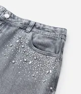 Pantalón de jean modelo wide leg color gris, con cintura tradicional, bolsillos funcionales y detalle de aplicaciones de brillos en la parte superior.