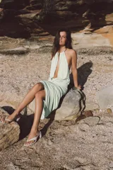 Vestido largo color verde menta, con escote halter pronunciado y detalle de choker metálico. Cuenta con fajín drapeado en la cintura, diseño sin mangas y falda fluida.