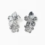 Par de caravanas de metal plateado con diseño de doble flor superpuesta, con acabado texturizado y brillante.