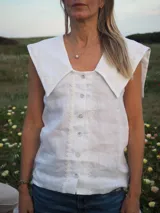 Blusa sin mangas de lino color blanco, con cuello marinero grande y detalles de encaje en el cuello y a lo largo de la botonadura frontal.