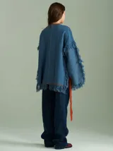 Sweater oversize de lana con diseño de trenza central, detalles en tejido cuadrillé y terminaciones desflecadas. Presenta mangas acampanadas, cuello a la base y aberturas laterales con tiras ajustables.