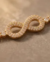 Pulsera de acero con baño de oro, diseño de infinito adornado con circonias y cadena tipo tenis.