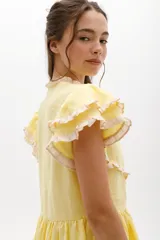 Vestido midi de lino blanco con diseño de broderie, cuello alto, cierre frontal con botones y volados decorativos en los hombros y el cuerpo.