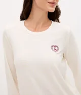 Pijama largo de mujer confeccionado en tejido peach touch, compuesto por una blusa de cuello redondo y manga larga con pequeño bordado en el pecho, y un pantalón con cintura elástica. Presenta un sutil estampado de cuadros.