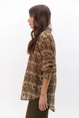 Camisa de manga larga con estampado de tapiz en tonos marrones, verdes y beige. Tiene cuello clásico y cierre frontal con botones.