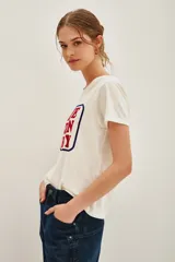 Remera de algodón blanca con cuello redondo y estampa frontal con el texto 'BLUE JEAN BABY' enmarcado en un recuadro negro.