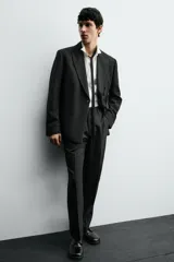 Pantalón de vestir negro con pliegues frontales, corte regular fit, bolsillos laterales y traseros de doble vivo con botón. Cierre frontal cruzado con cremallera y gancho metálico.