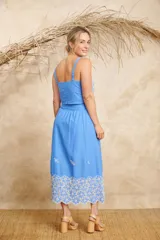 Conjunto de dos piezas compuesto por un crop top de breteles anchos y una pollera midi, ambos en color azul con detalles de bordado floral blanco en el ruedo y el lateral del top.