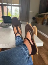 Ballerinas de gamuza color marrón oscuro con diseño tipo T-strap y detalles de costuras decorativas en color verde oliva. Cuentan con cierre de pulsera al tobillo y suela plana.