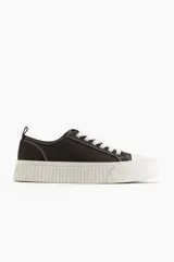 Zapatillas deportivas bajas de lona color marrón oscuro, con cordones blancos y suela de goma blanca con diseño acanalado.