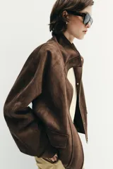 Chaqueta de tejido efecto ante color marrón, con cuello alto, cierre frontal con cremallera y botones a presión, manga larga y bolsillos de plastrón con solapa en el delantero.