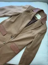 Tapado de lana color bordó con solapas y detalles en los bolsillos de cuero. Presenta cierre frontal con botones y diseño de líneas clásicas.