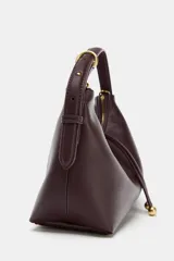 Bolso de mano tipo saca, color borgoña, con asa de mano ajustable y correa bandolera extraíble. Presenta un detalle de doble tira con terminaciones de bolas metálicas doradas en el frente.