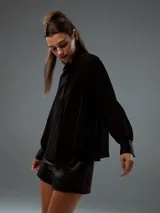 Camisa de tela semitransparente color negro, con cuello clásico, cierre frontal de botones y mangas largas con puños ajustados.