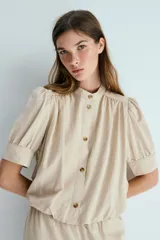 Blusa de sarga suave en color beige, con cuello mao, botonadura frontal con botones carey, mangas cortas abullonadas con puños y bajo globo.