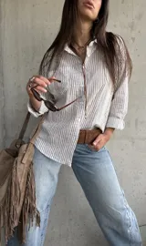 Camisa de corte oversize, con diseño a rayas verticales marrón sobre fondo blanco, manga larga, cuello camisero y bolsillos frontales.
