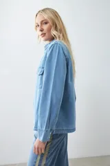 Camisa de jean celeste con cuello clásico, cierre frontal con botones a presión, dos bolsillos con solapa abotonada en el pecho y mangas largas con puños abotonados.