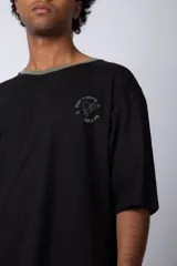 Remera de corte oversize en color beige, con cuello redondo en contraste negro y una manga en color negro. Presenta un pequeño estampado circular en el pecho con la frase 'Don't worry, be happy'.