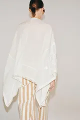 Blusa tipo capa de algodón con escote en pico y cierre frontal con botones. Presenta mangas largas amplias y diseño con bordados florales a tono, con bajo asimétrico.