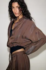 Chaqueta de cuello solapa y manga larga, confeccionada en tejido jacquard con diseño de rayas verticales. Presenta cierre frontal con botones y bajo ajustable mediante cordones.
