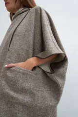 Ruana color crudo de lana fina sin teñir, con capucha, bolsillos y terminaciones envivadas. Tiene un broche para usar cerrada. Es una prenda oversize sin forro, cómoda, versátil y fácil de combinar.