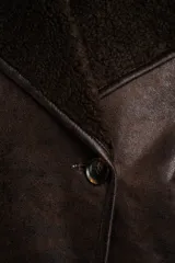 Campera tipo gamulan de corte oversize, color marrón oscuro con interior y solapas de corderito al tono. Presenta cierre frontal y mangas largas.