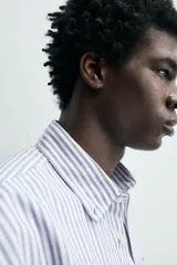 Camisa de corte regular fit confeccionada en tejido de algodón con diseño de rayas verticales. Presenta cuello abotonado, manga larga con puños abotonados, bolsillo plastrón en el pecho y cierre frontal con botones.