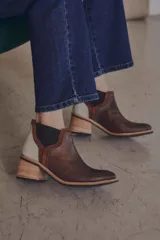 Botineta de diseño tricolor con cuerpo en tono beige, panel elástico lateral negro y talón con textura símil reptil en color marrón. Presenta un taco cuadrado robusto de color negro.