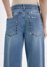 Jeans de denim celestes de tiro medio, diseño de corte recto y amplio con detalles de tachuelas en los bolsillos delanteros.
