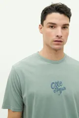 Remera de manga corta color verde agua con estampado gráfico en la espalda que incluye texto y motivos playeros. Confeccionada en algodón con calce regular.