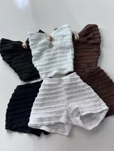 Conjunto de dos piezas color marrón, compuesto por un top strapless con frunces y detalle de hebilla metálica en el centro, y un short ajustado con diseño fruncido en los laterales.