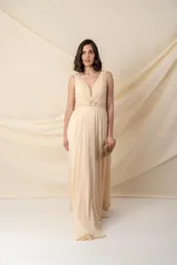 Vestido largo de gasa color champagne, con escote en V profundo y breteles anchos. Presenta una faja bordada con pasamanería y piedras en la cintura.