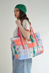 Bolso grande tipo tote bag, capitoneado a mano con estampado de patchwork multicolor. Tiene mangos resistentes con detalles de cinta rosa y beige. Cuenta con tres bolsillos interiores y cinco exteriores.