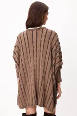 Sweater de punto con diseño de trenzas verticales, color crudo y camel, con bolsillos frontales y detalle de logo bordado. Presenta un corte holgado y mangas largas.