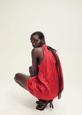 Vestido corto de cuello halter con diseño recto y fruncido en la parte superior. Presenta un cierre de lazo en la nuca y un acabado con textura sutil.