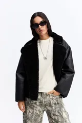 Campera de estilo aviador en color negro, confeccionada en material tipo gamuza con interior de corderito sintético. Presenta un diseño de corte holgado, cuello amplio con solapas y cierre frontal.