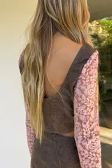 Top corto confeccionado en cuero negro con mangas largas de encaje floral. Presenta escote en V, diseño entallado con costuras decorativas y cierre frontal mediante botones metálicos.