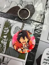 Llavero redondo con imagen de personaje de anime con pelo negro y campera naranja.