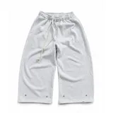 Pantalón de jogging gris melange de corte baggy, confeccionado en algodón. Presenta cintura elástica con cordón largo ajustable, bordado decorativo en la pierna izquierda y botones metálicos en la parte inferior de la botamanga para ajustar el ancho.