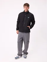 Campera reversible con cuello alto y cierre frontal. Un lado presenta tejido de polar con estampado geométrico en tonos verdes y bolsillo con cierre en el pecho, mientras que el otro lado es de nylon. Cuenta con puños elásticos y bolsillos laterales.